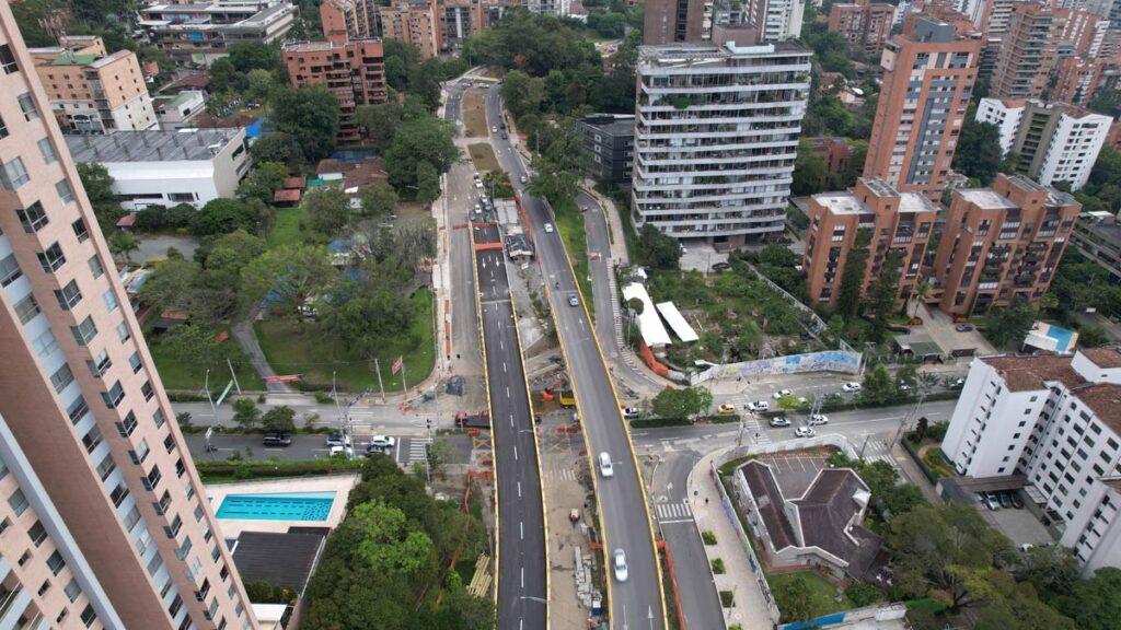 Vista aérea urbana con edificios altos, carretera elevada en construcción y áreas verdes.