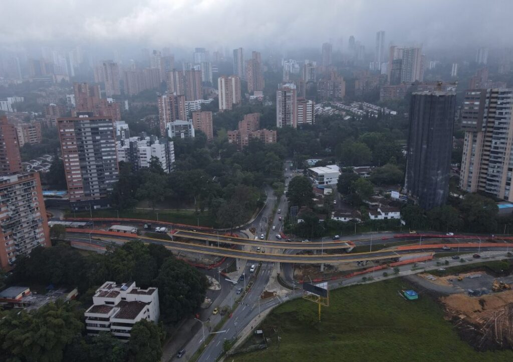 Aerial view of a cloudy cityscape with tall buildings, greenery, and road under construction.