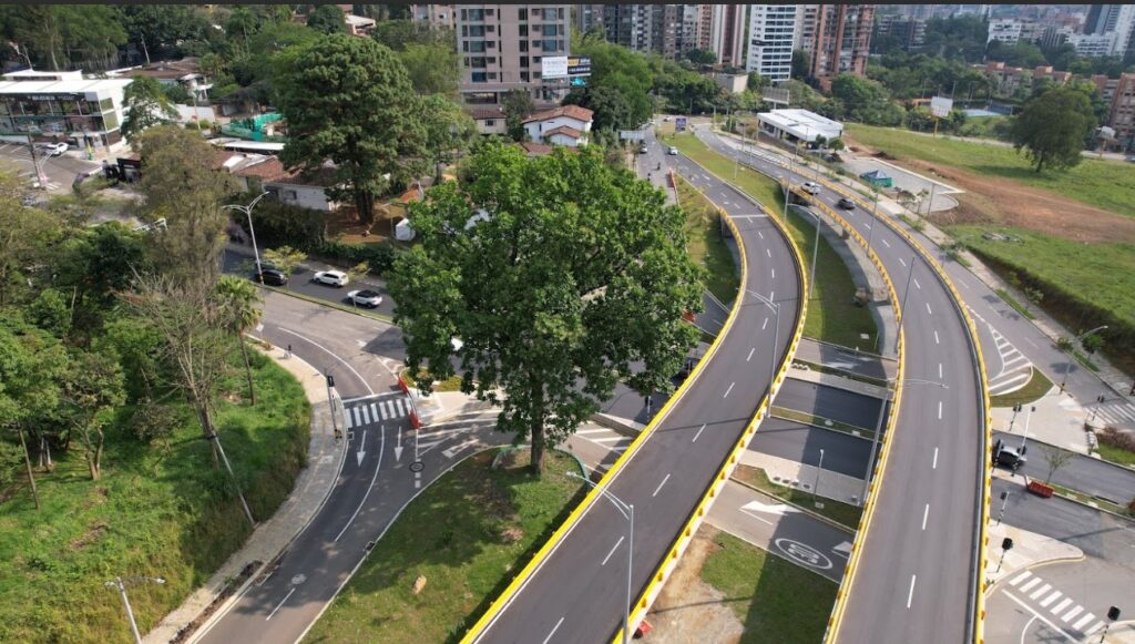 Carretera moderna con intersección, áreas verdes, edificios y vehículos en movimiento.