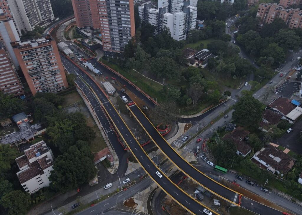 Vista aérea de intersección urbana con puente, edificios altos y zonas verdes circundantes.